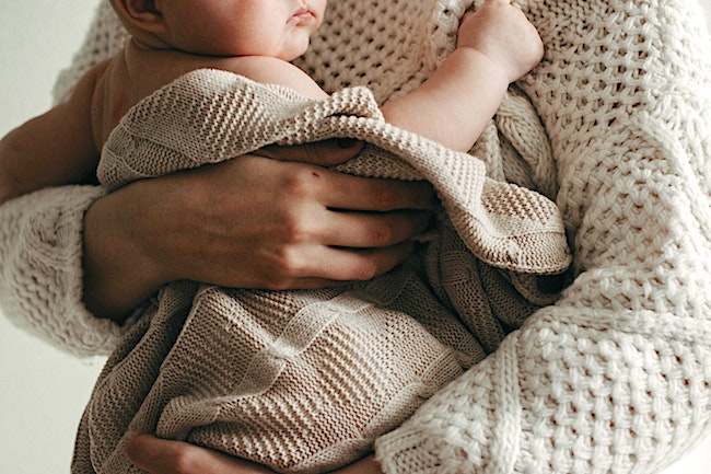 Person in Strickpullover hält Baby im Arm